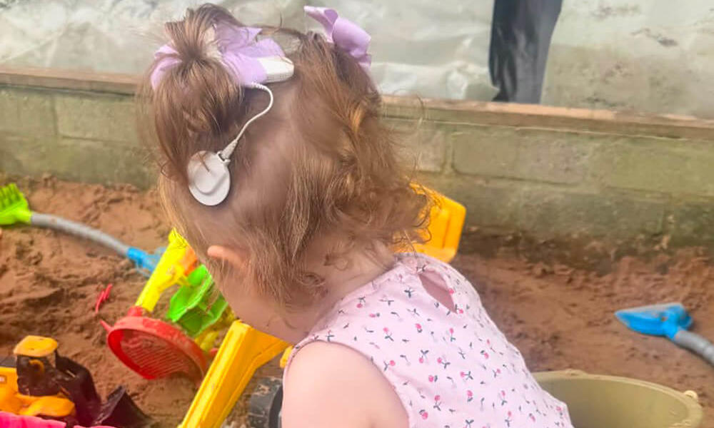 Young girl, wearing a cochlear implant, playing in the sand pit at the d/Deaf playgroup