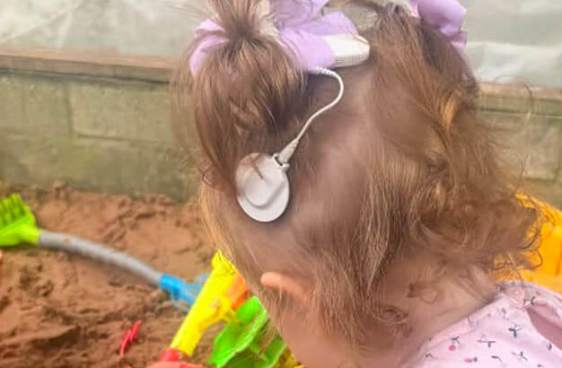 Young girl, wearing a cochlear implant, playing in the sand pit at the d/Deaf playgroup